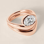 Three-quarter angled view of Liora oval bezel engagement ring stacked with a diamond contour wedding band in 18K rose gold.