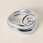 Three-quarter angled view of Liora oval bezel engagement ring stacked with a diamond contour wedding band in white gold or platinum.