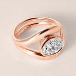 Three-quarter angled view of Liora oval bezel engagement ring stacked with a plain gold contour wedding band in 18K rose gold.