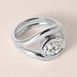 Three-quarter angled view of Liora oval bezel engagement ring stacked with a plain contour wedding band in white gold or platinum.