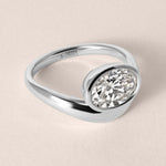 Three-quarter top view of Liora oval bezel engagement ring in white gold or platinum showcasing the fluid split-band shank.